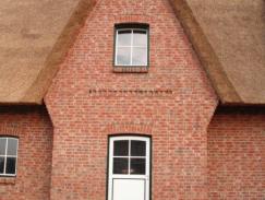 Hausansicht Einfamilienhaus mit Reetdach mit Haustür und Fenstern in grün/weiß 