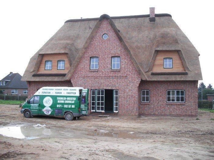 Hausansicht Einfamilienhaus mit Reetdach mit Terrassentür und Fenstern in grün/weiß 