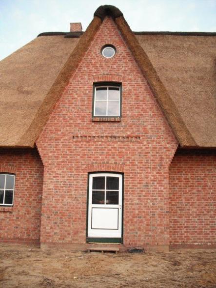 Hausansicht Einfamilienhaus mit Reetdach mit Haustür und Fenstern in grün/weiß